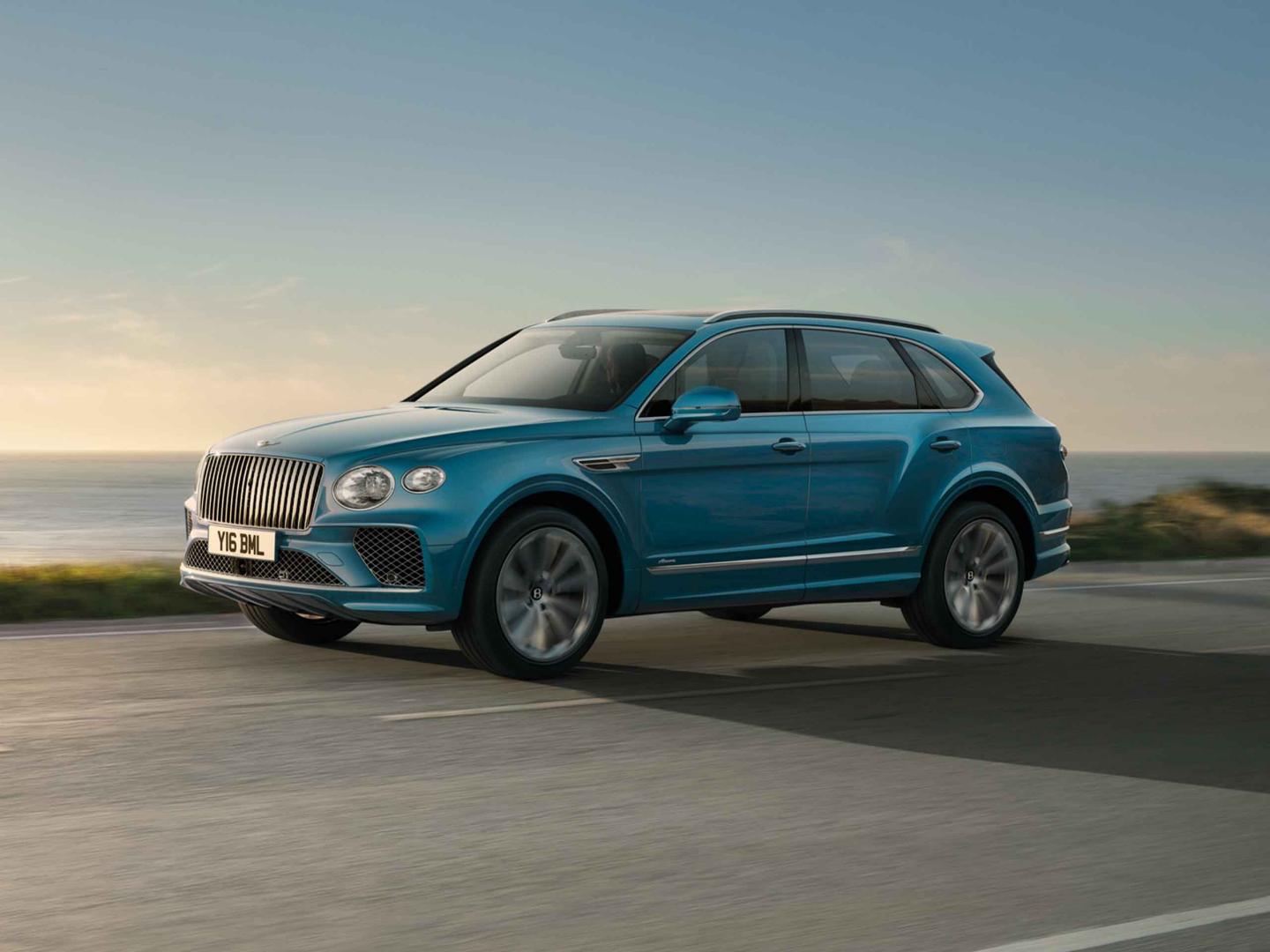Bentley Bentayga Azure side view in Topaz blue / Kingfisher- by Mulliner colour, featuring 22 inch Painted and Diamond Turned Wheel, driving along sea side.